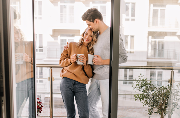 A couple stands on their apartment balcony enjoying coffee knowing their Selective renters insurance is protecting their possessions.